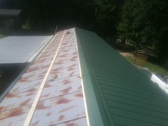 Old rusted panels beside newly installed green metal roofing — Wind Damage Roof Repair by Roofing Brothers in Clyde